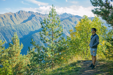 One tourist in shorts and a sweatshirt standing on top of a cliff on the background of trees and watching the beautiful views. Beautiful moment a miracle of nature. Mestia