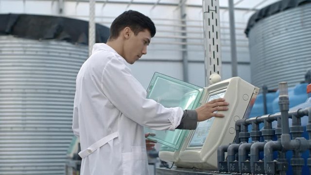 PAN of young male agricultural chemist in lab coat operating fertigation machine in large commercial greenhouse with hydroponic system
