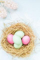 Colored Easter eggs in the nest and flowers. Space for text. Festive light Easter decoration. Easter concept.