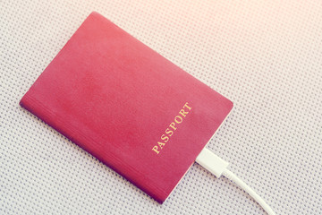 Red Passport with a white cable connected on a gray textile background in the sunlight. Toned
