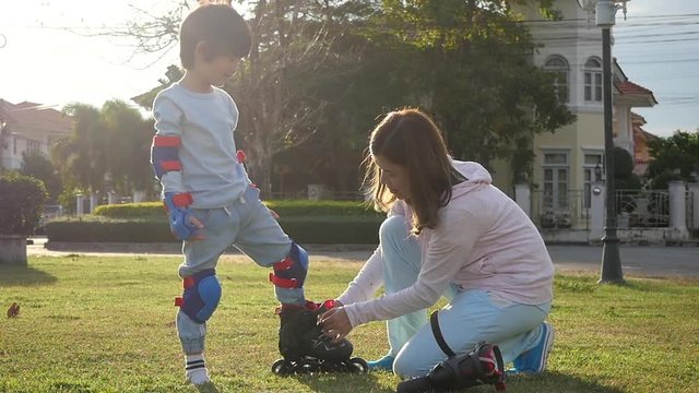 Asian mother helping her son putting his roller skates on enjoying time together in the park slow motion 