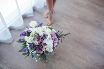 Beautiful wedding bouquet in a decorative bucket or box and the bride's legs on a white terrace background.