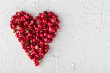 Pink peppercorns in a heart shape on white background