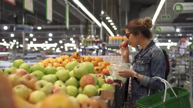 Woman in the stylish glasses chooses oranges in the supermarket