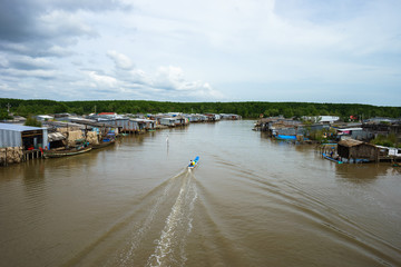 Landscape in Ca Mau with wooden boat running along floating village in Mekong delta, South Vietnam