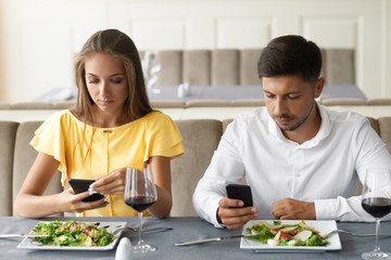 Couple Using Phones On Dinner In Restaurant.