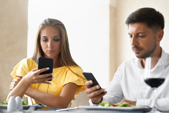 Couple Using Phones On Dinner In Restaurant.