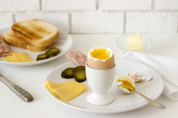 Breakfast with soft-boiled egg, bread toast, ham, cheese and canned cucumbers. Rustic style.