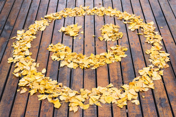Smiley drawn with yellows leaves on a wooden ground in autumn,