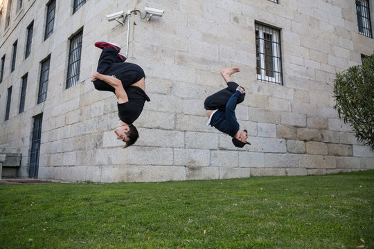 Two young men doing a side flip or somersault while they practicing parkour on the street.