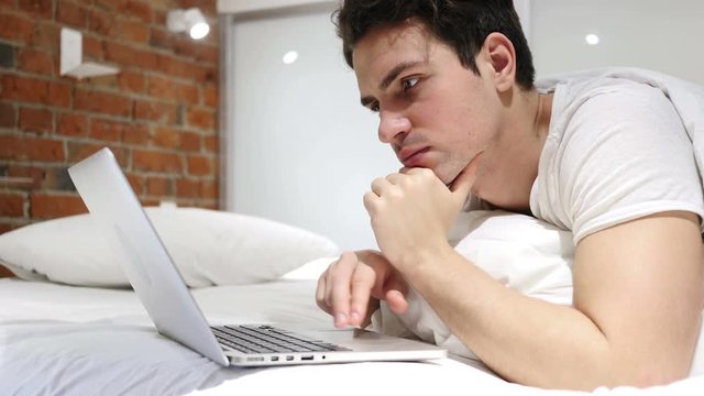 Thinking Pensive Man in Bed Working on Laptop at Night