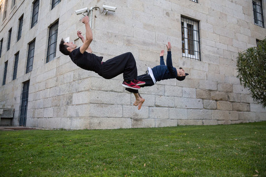 Two young men doing a side flip or somersault while they practicing parkour on the street. 