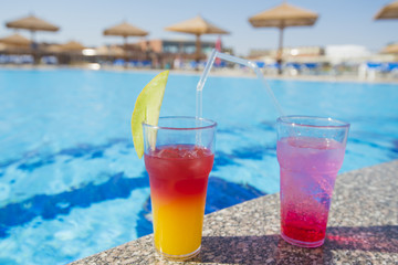 Two cocktail drinks by a tropical swimming pool