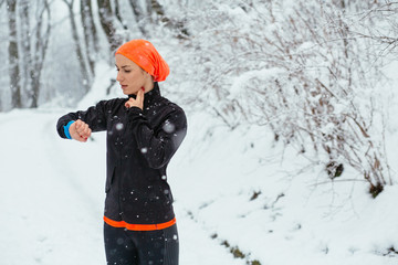 Young woman jogger checking heart rate after run in snowy winter park, outdoor. Healthy lifestyle...