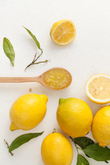 Fresh lemons with leaves and chopped lemons and sugar in a bowl on a white background.