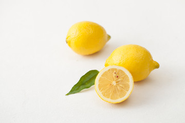 Lemons with leaves and a sliced lemon on a white concrete background.