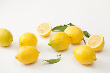 Naklejka na ściany i meble A bunch of lemons with leaves and sliced lemons on a white concrete background.