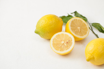 A bunch of lemons with leaves and sliced lemons on a white concrete background.