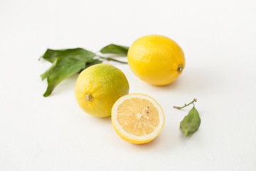 A bunch of lemons with leaves and sliced lemons on a white concrete background.