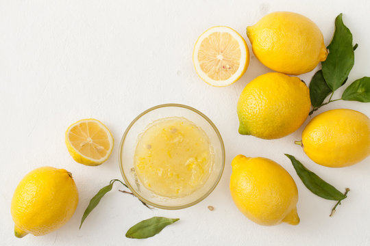 Fresh lemons with leaves and chopped lemons and sugar in a bowl on a white background.