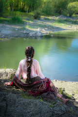 Beautiful woman boho, sitting on a rock on the river bank.