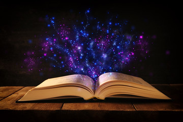 image of open antique book on wooden table with glitter overlay.