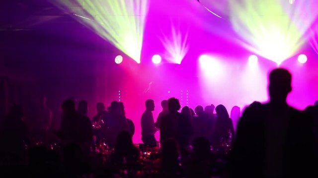 a youth party in a restaurant or a nightclub, banquet tables with alcohol and food against the background of silhouettes of dancing people, stage light and purple fill