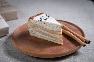 piece of cake with white chocolate and cinnamon sticks lying on a wooden plate next to the box with a gift