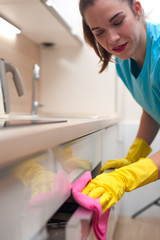 Young charming woman wipes kitchen equipment from dust with rag. Cleaning in the kitchen