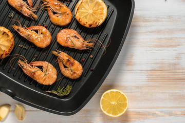 Grilled shrimps on a grill frying pan with lemon, paprika, spices and herbs. Wooden background.