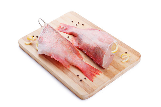 Two raw red sea perches on a wooden cutting board on white background