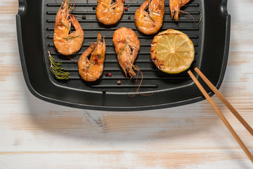 Grilled shrimps on a grill frying pan with lemon, paprika, spices and herbs. Wooden background.