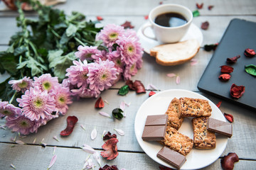A Cup of coffee,note book , cracker, cookie, biscuit, lupins flowers on a wooden table.