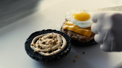 Closeup of chef cook grilled black burgerwith sauce and eggs on kitchen board