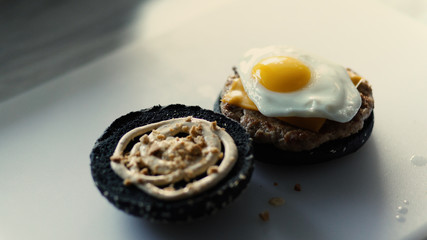 Closeup of grilled black burgerwith sauce and eggs on kitchen board
