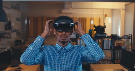 Young African American black male professional puts on augmented reality AR hololens headset in modern office. 4K UHD - Powered by Adobe