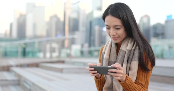 Woman playing game on smart phone in city