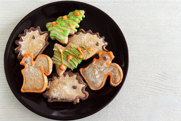 Christmas figured gingerbread on a dark plate on a white wooden surface, top view