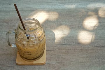 A glass of iced coffee on a wooden plate and wooden table with a sunshine of morning time.