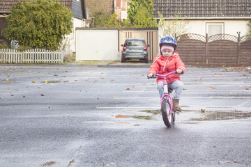Happy child riding a bicycle in the fall. Cute little girl in safety helmet riding a bike outdoors. Little girl on a red bicycle. Healthy preschool children activity.
