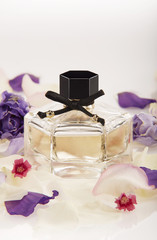 Small glass bottles of perfume surrounded with flowers on a white background with reflections