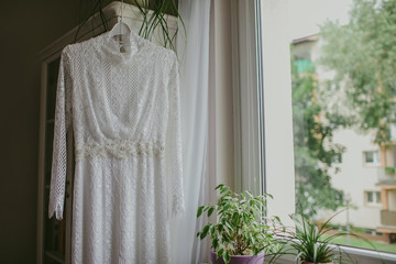 White wedding dress hanging on wardrobe next to the window.