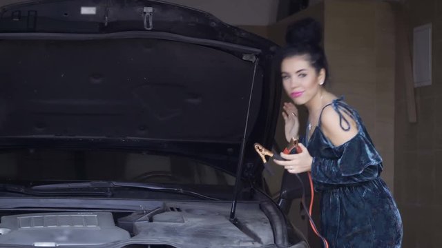 Young woman plays with jumper cables standing near car in garage