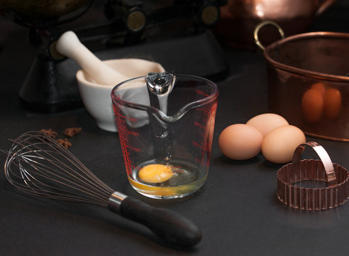 raw eggs prepared for whisking, a whisk, white mortar and vintage scale with apples and baking copper shape  