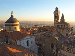 Fototapeta na wymiar Bergamo, Italy. The old city. Aerial view of the Basilica of Santa Maria Maggiore and the chapel Colleoni during the sunset. In the background the Po plain
