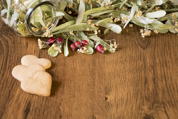 Healthy concept view of dry linden flowers, red rose hips and honey cookies on wooden background.