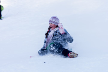Fototapeta na wymiar Girl in winter clothes is riding on a snow slide.