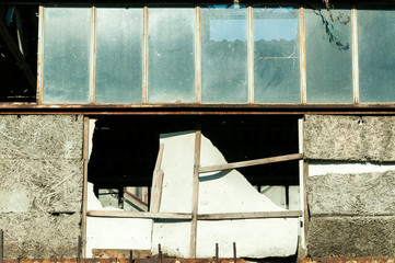 Damaged warehouse exterior wall with broken glass windows close up