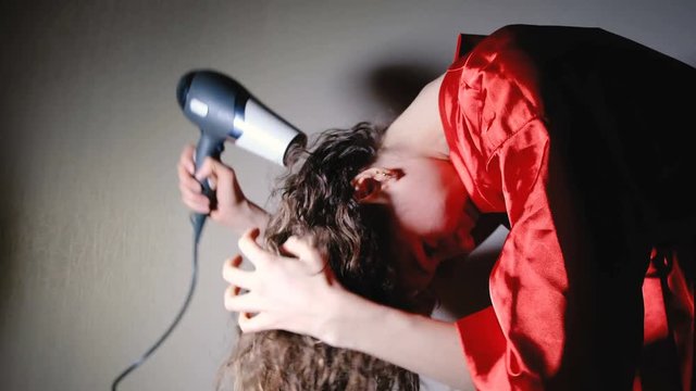 Young woman with brown hair drying hair the tilt of the head with electric blowdryer at home, 4K.