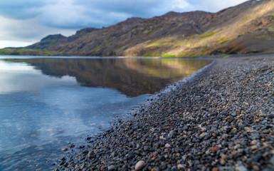 Curved stone beach of a lake with mountains in the background and beautiful reflections